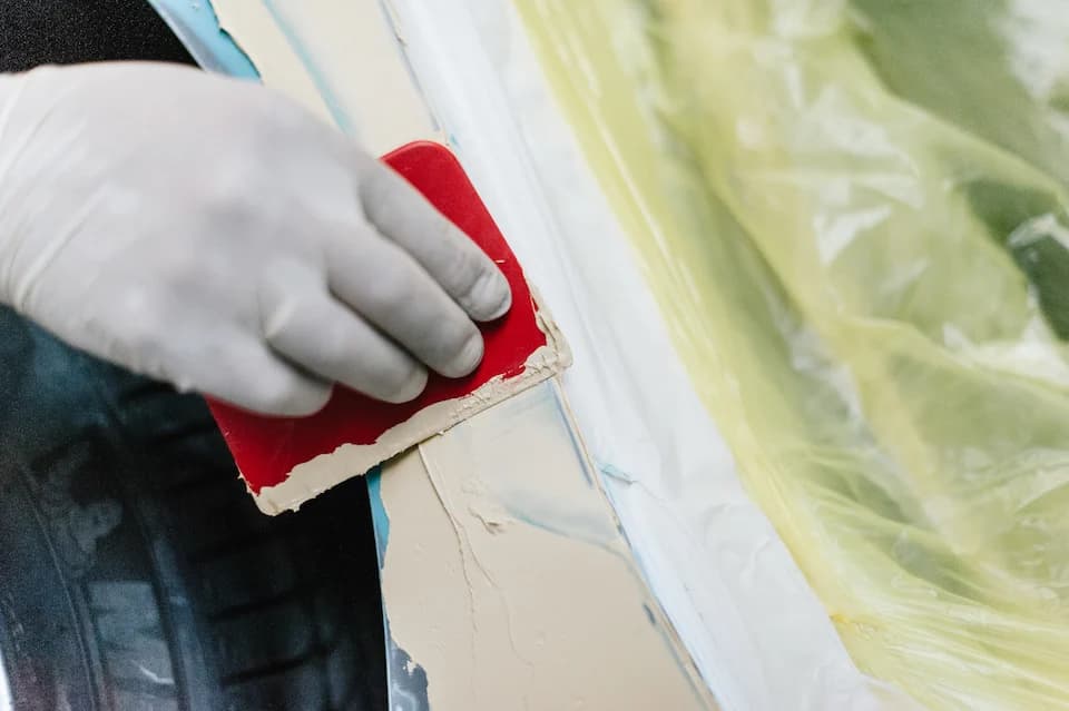 Behandschuhte Hand bereitet eine abgeklebte Fläche für die Lackierung vor