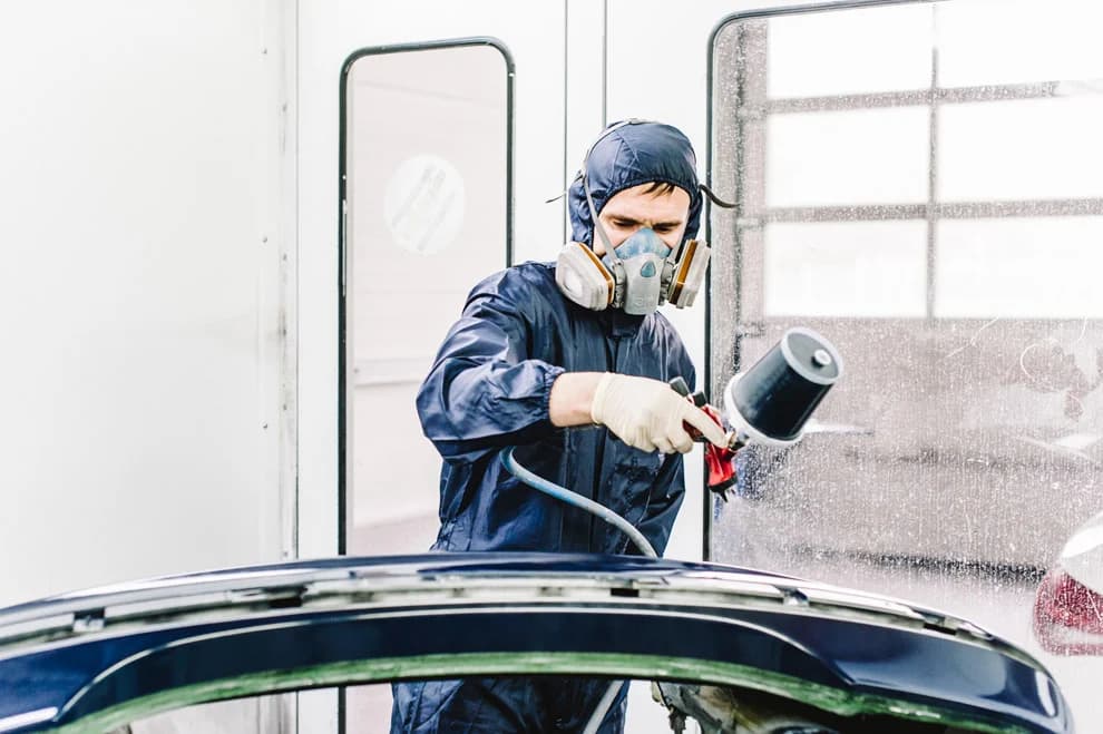 Lackierer lackiert die Motorhaube eines Fahrzeugs in der Kabine